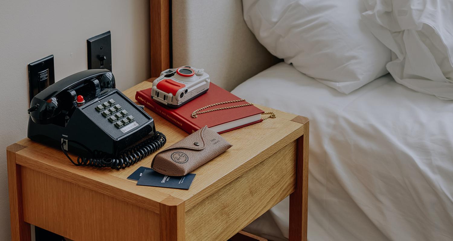 A bedside table with old-school phone, camera, and journal.