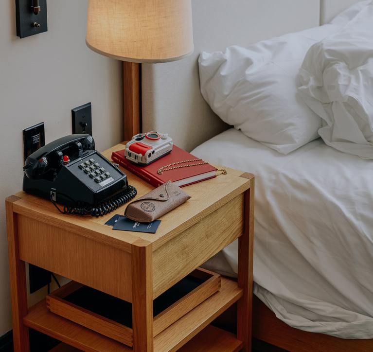 A bedside table with old-school phone, camera, and journal.