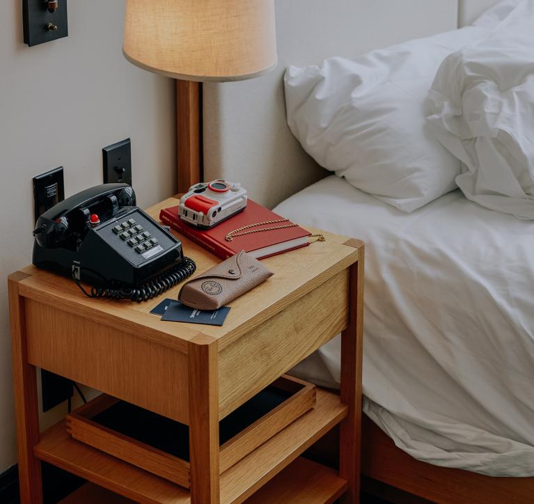 A bedside table with old-school phone, camera, and journal.