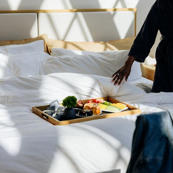 Wooden room service tray with bread, cheese, and fruit on a bed at Shinola Hotel.